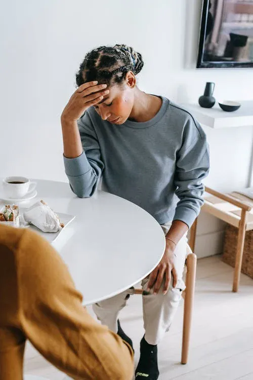 Une femme assise devant un café se tient le front dans la main - Mal de tête - Migraine - Hypnose à Nantes