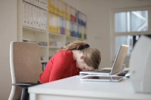 Une femme a posé sa tête sur son ordinateur portable et a fermé les yeux. Motivation - équilibre vie professionnelle et vie privée - Coaching professionnel - Coaching de vie