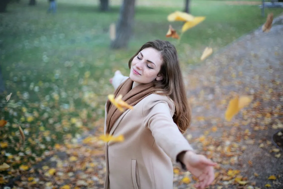 Une femme, les yeux fermés, sourit en ouvrant les bras dans un parc - Se débarrasser de ses migraines - Sérénité - Hypnose