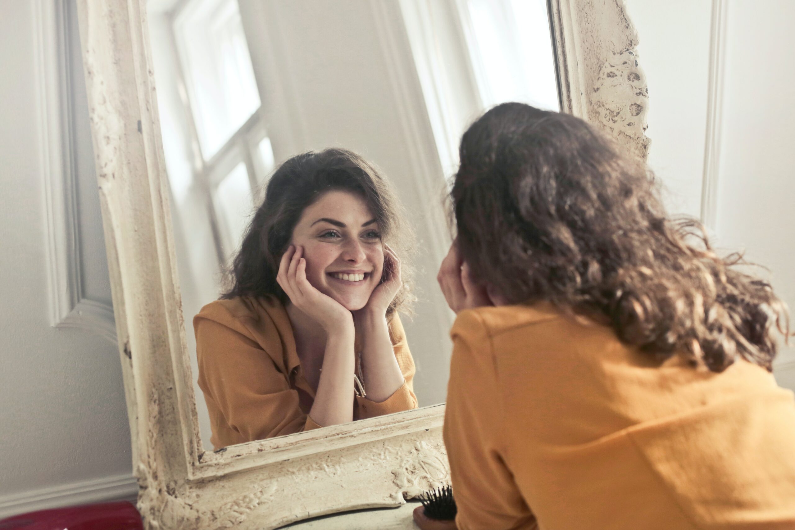 Une femme se regarde dans un miroir en souriant - bienveillance - hypnose - coaching de vie - coaching personnel