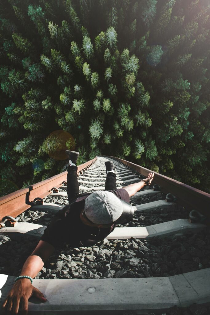 Plongée vertigineuse d'un homme accroché à des rails de chemin de fer et qui risque de tomber de très haut. Travailler son estime de soi pour oser être heureux.