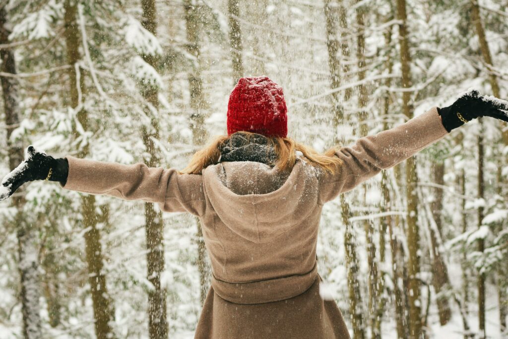 Une femme de dos écarte les bras sous la neige - Comment prévenir la dépression hivernale ? - Hypnose et coaching de vie