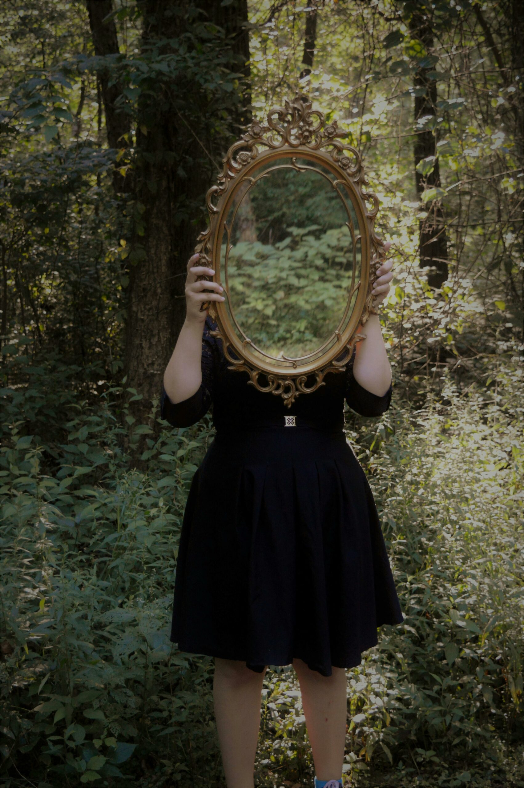 Une femme tient un miroir qui cache son visage et renvoie le reflet de la forêt qui l'entoure - Image de soi - Améliorer son estime de soi