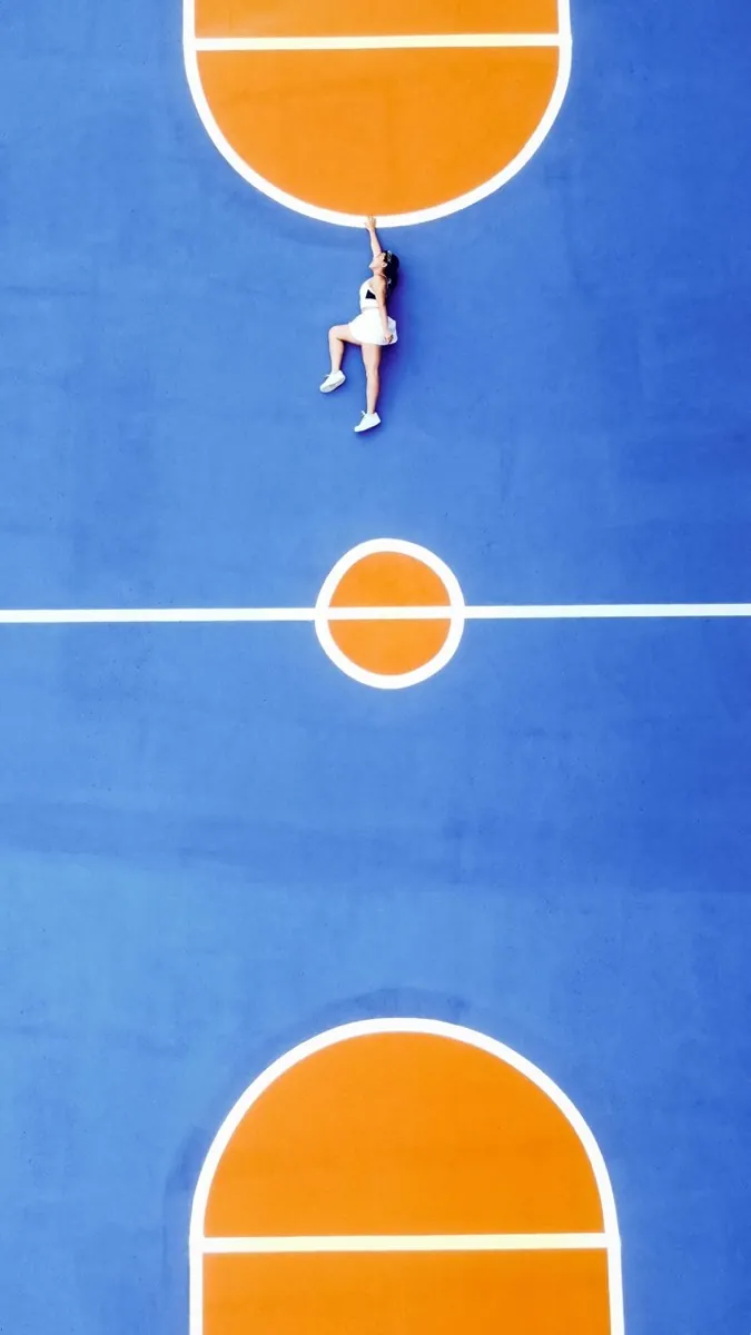 Une femme en jupe de sport semble suspendue au haut d'un terrain de sport stylisé sur fond bleu avec des zones de but oranges - Confiance en soi - Coaching de vie - Sylvie Rauwel - Nantes
