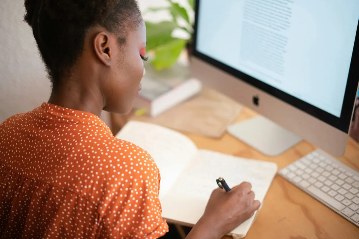 Une femme assise devant son ordinateur, écrit à la main sur un cahier - Confiance en soi - Coaching de vie - Sylvie Rauwel - Nantes