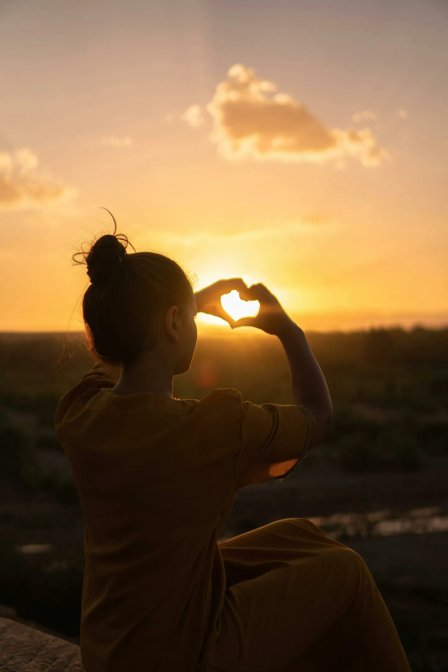 Un coucher de soleil vu entre les doigts d'une femme qui forment un coeur - Amour de soi - Coaching de vie - Sylvie Rauwel - Nantes